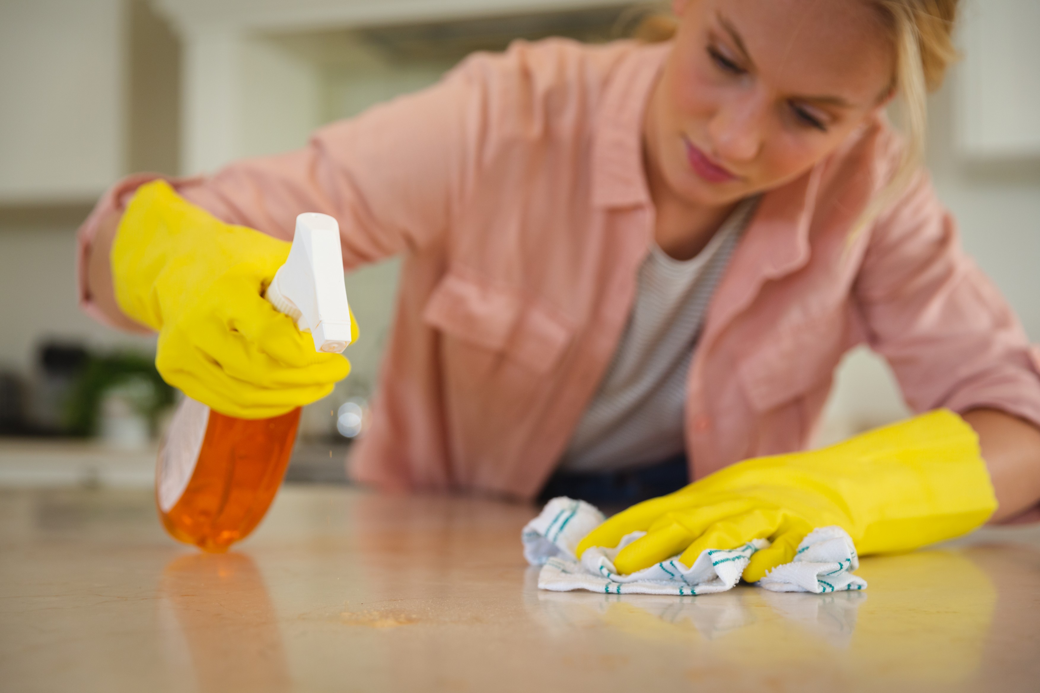 Caucasian woman wearing rubber gloves cleaning kitchen worktop with cloth and spray