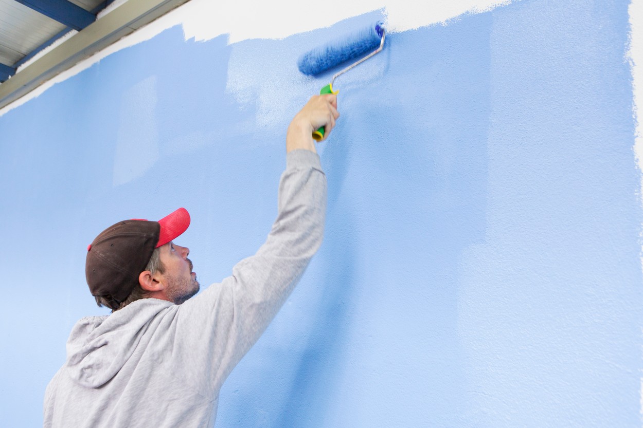 Rear view of man painting wall blue