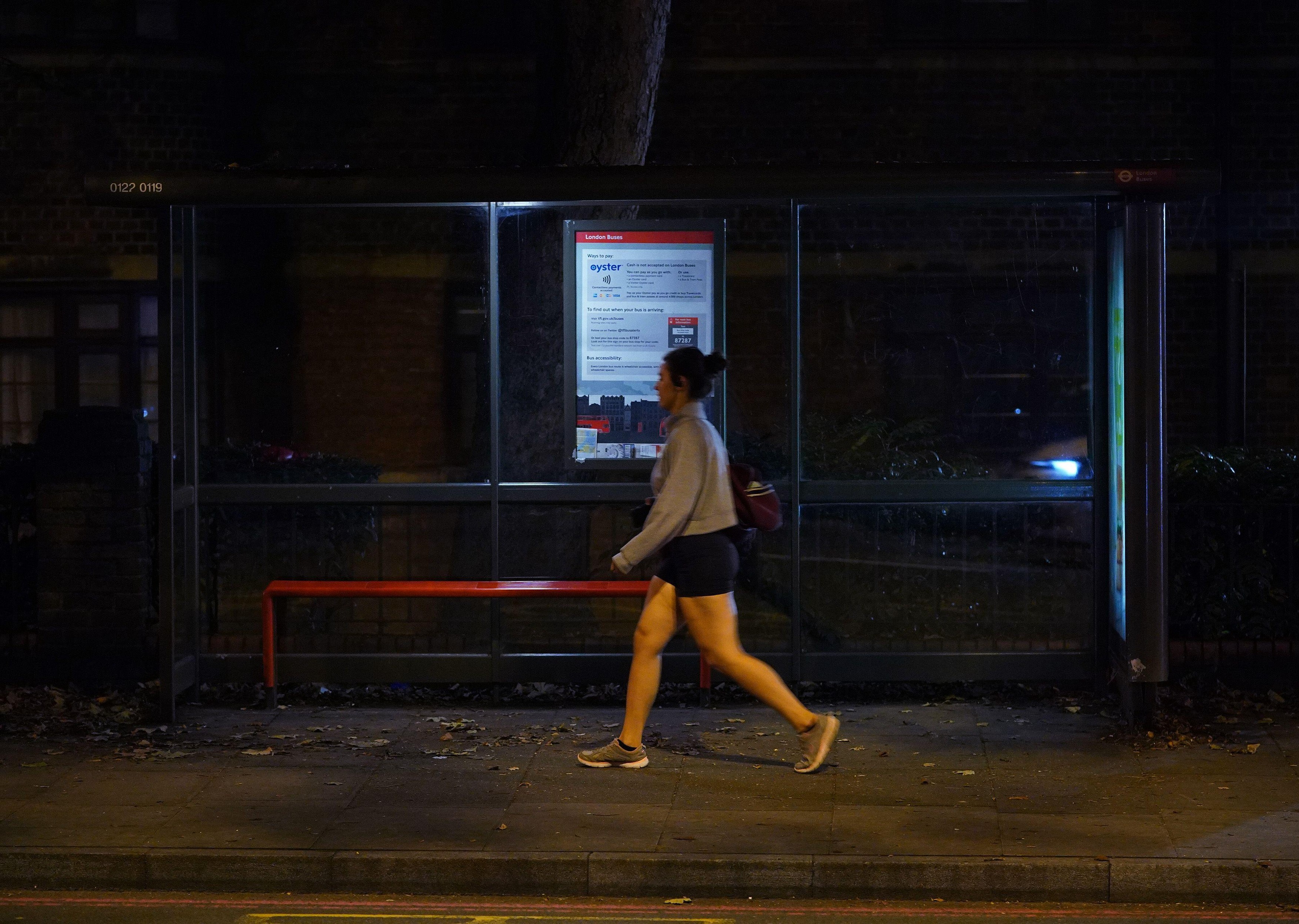 A woman walking alone after dark past a bus stop on Poynders Road in Clapham, south London, close to where Sarah Everard was abducted from the street by being falsely arrested by police officer Wayne Couzens in March. Picture date: Friday October 1, 2021.