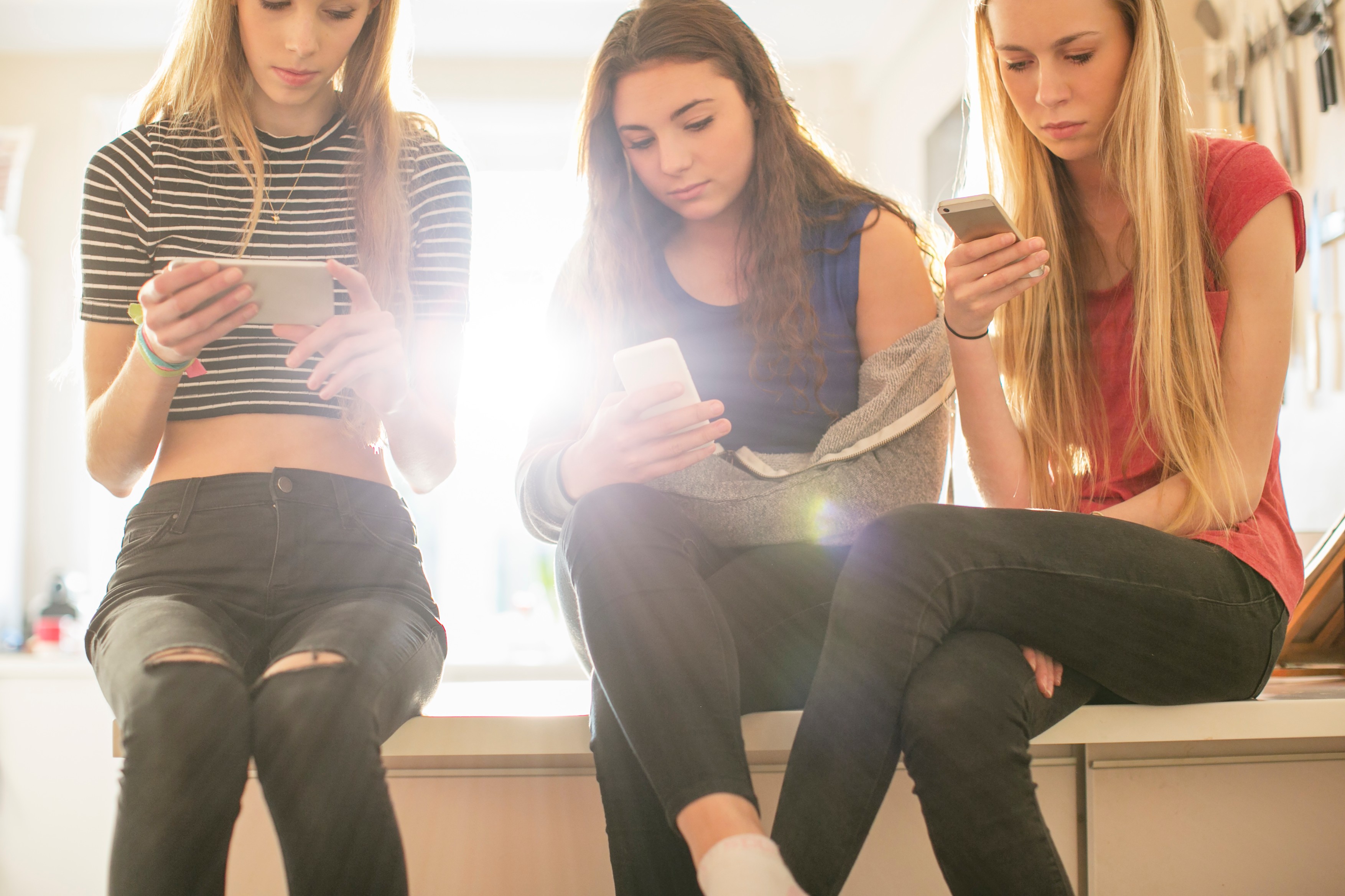 Teenage girls texting with cell phones in kitchen