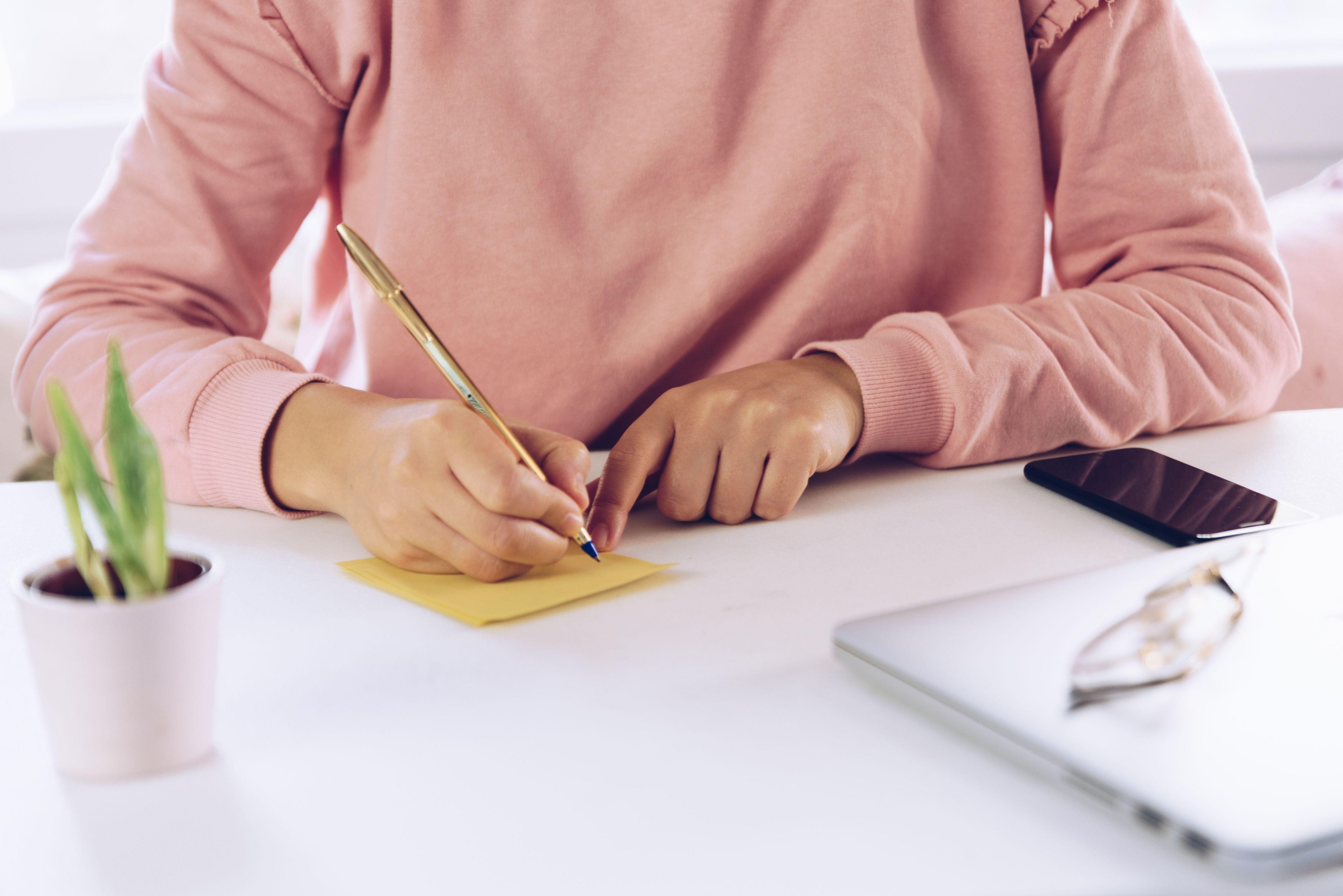 Woman hands writing a note on a white marble desk.