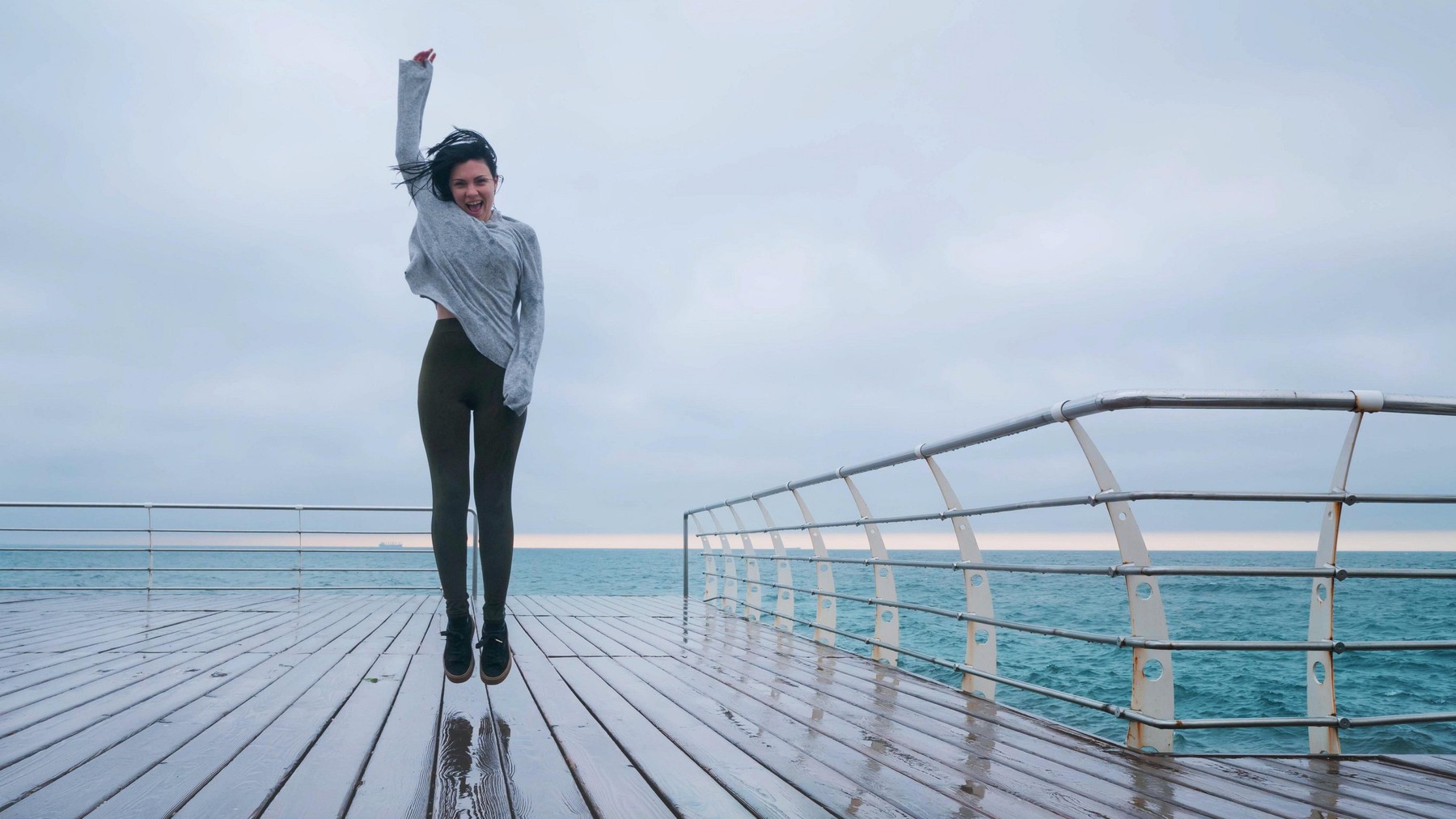 Beautiful young brunette dancing on the seashore or ocean in sportswear in the rain.