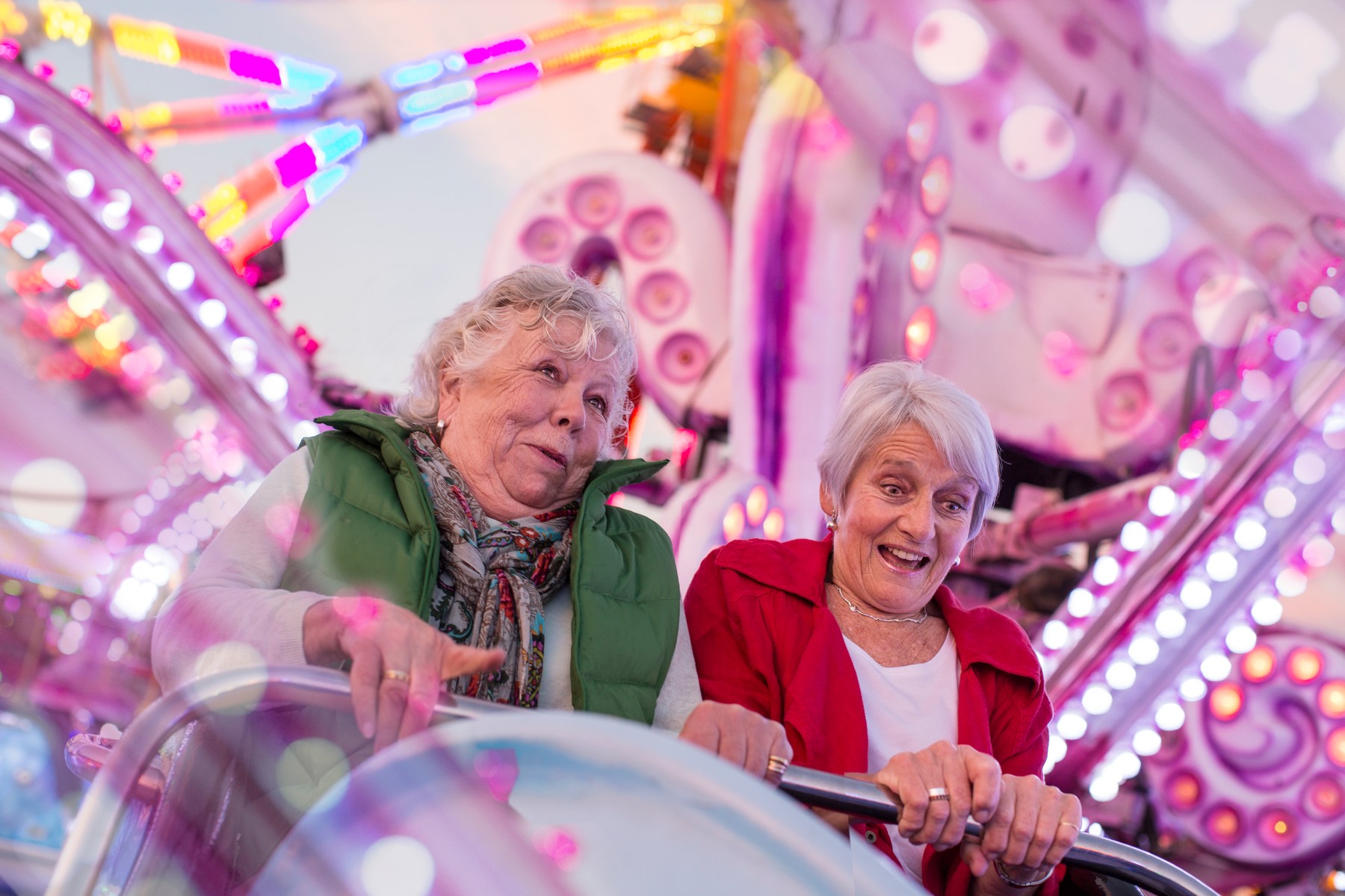 Two senior women riding roller-coaster at fairground