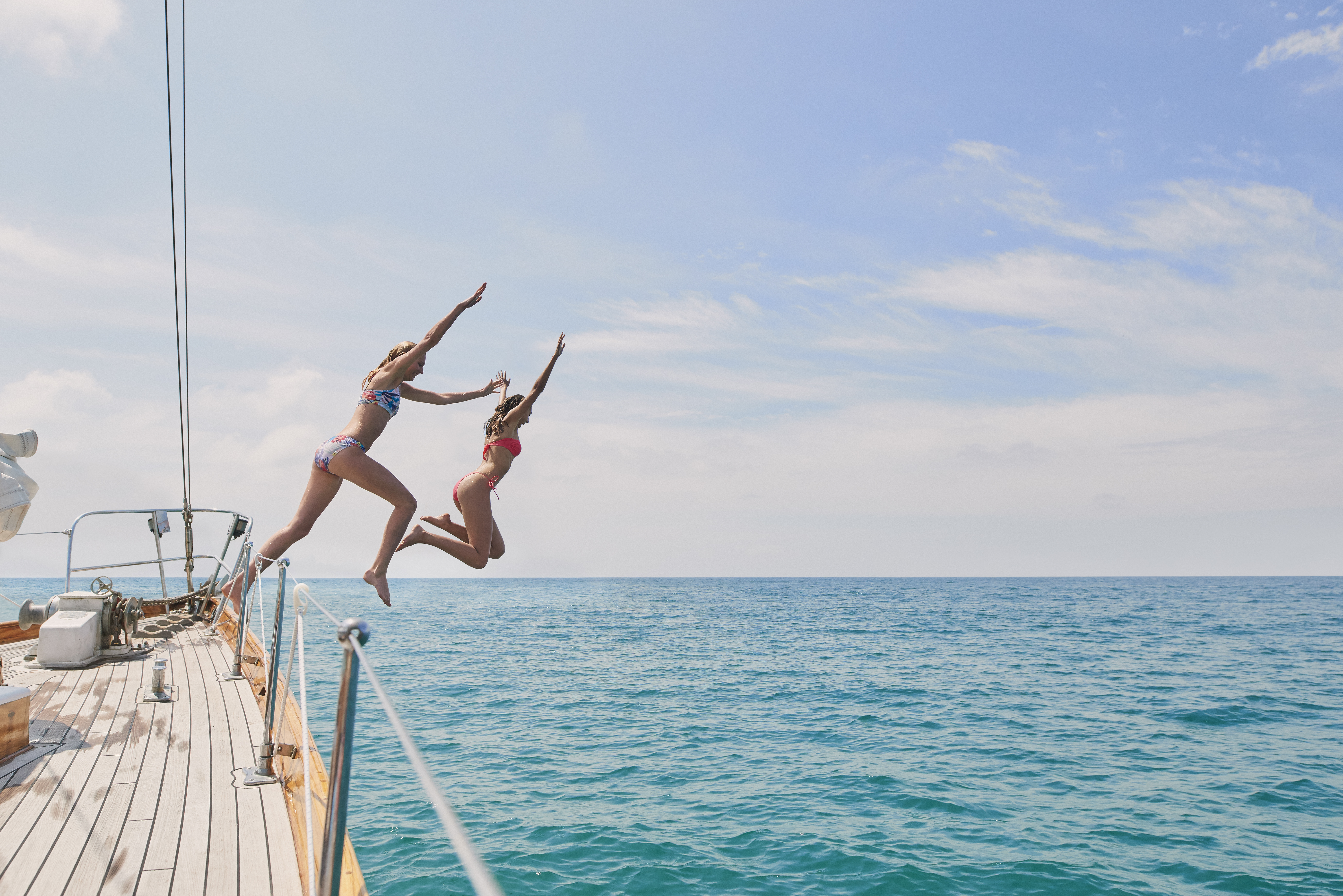Beautiful,Girl,Friends,Jumping,Into,Blue,Sea,From,Luxury,Wooden