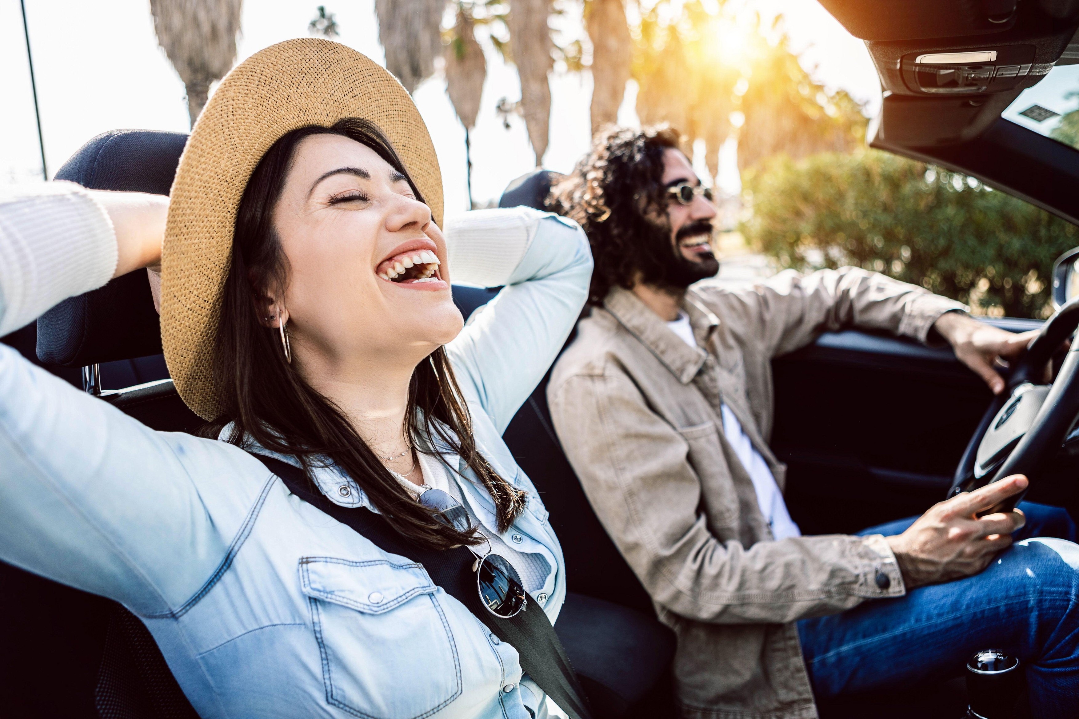 Happy young couple laughing together while driving a convertible car on holidays