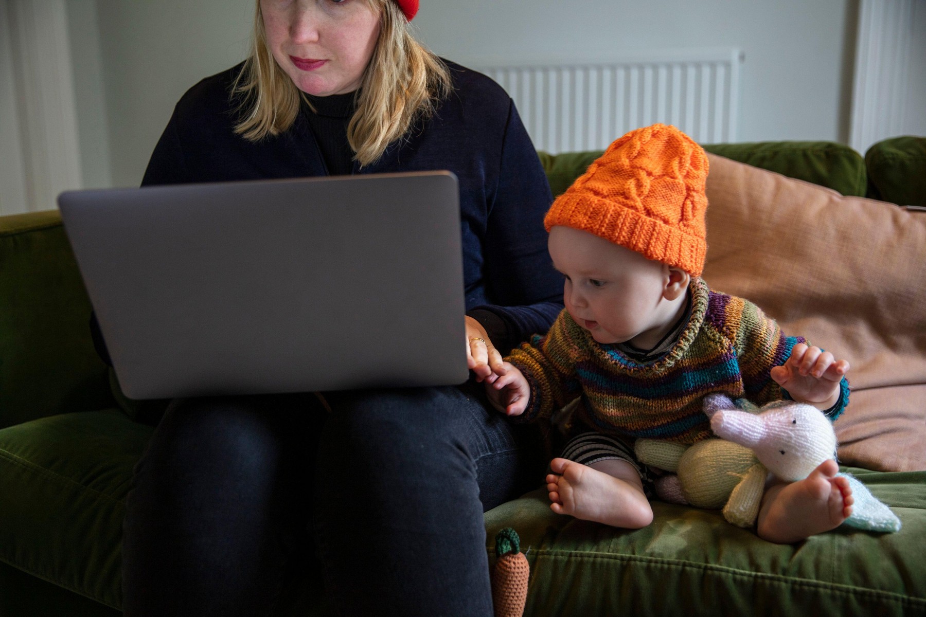 A young mother working from home on a laptop with a baby by her side