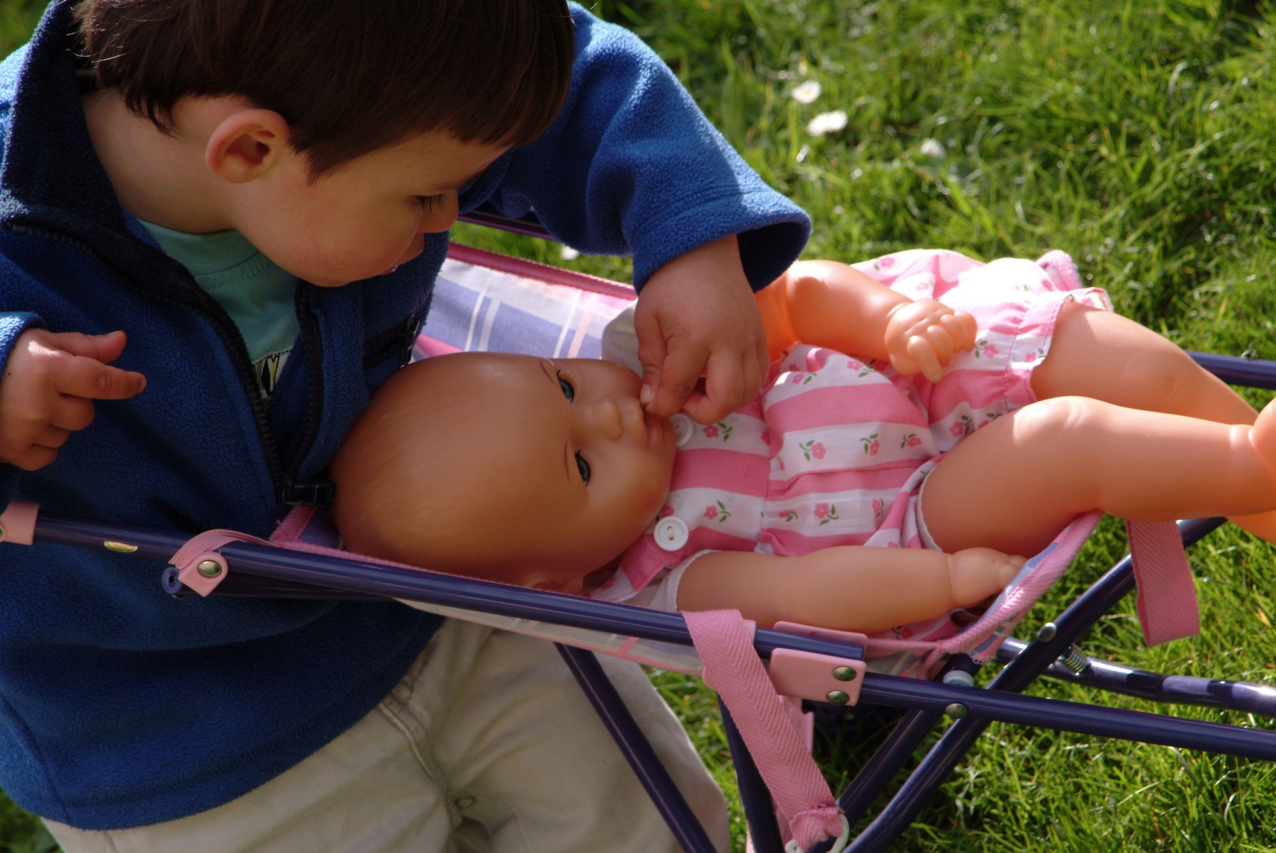 Little boy playing outside with a doll and a pushchair