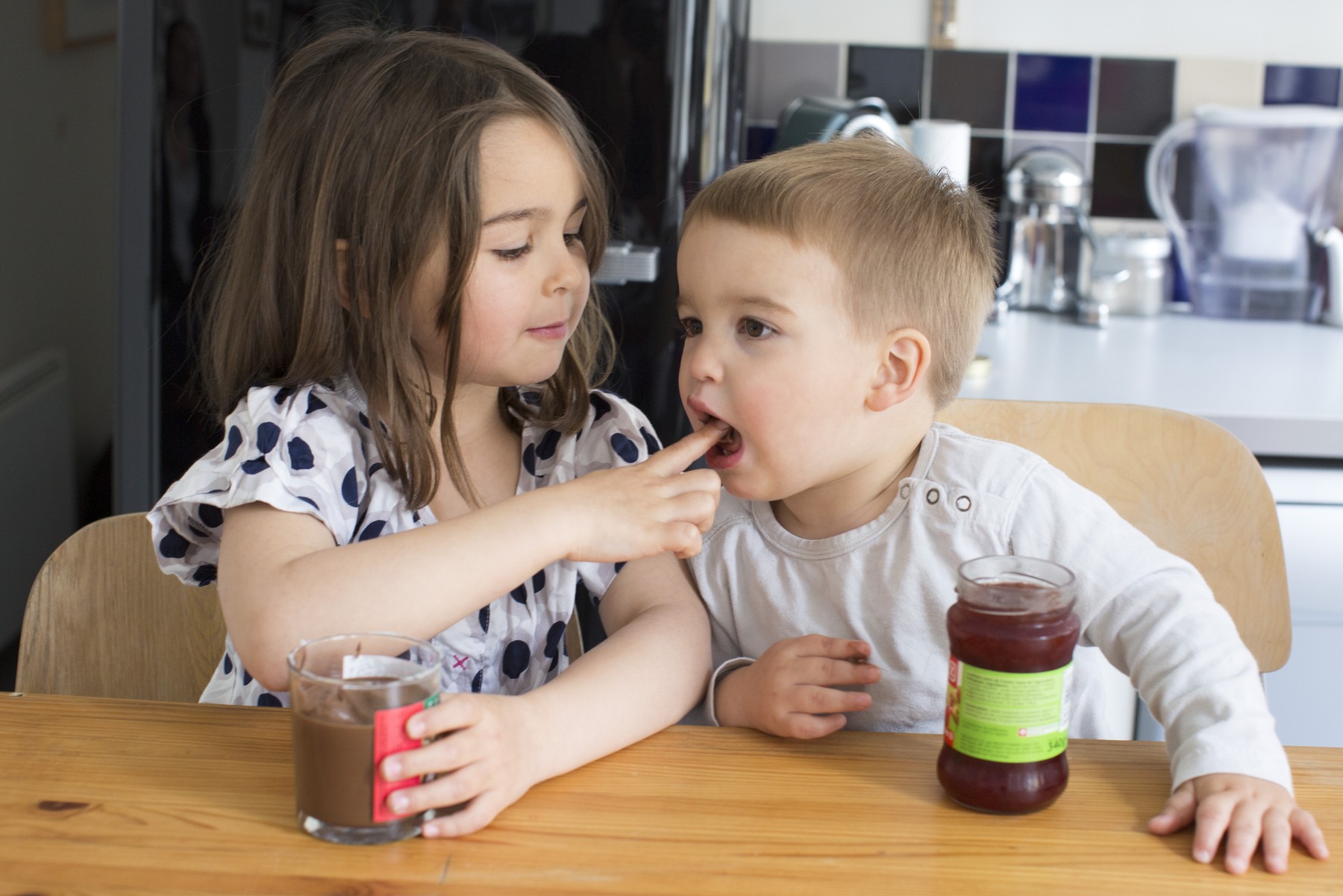 Young siblings tasting contents of jars with their fingers