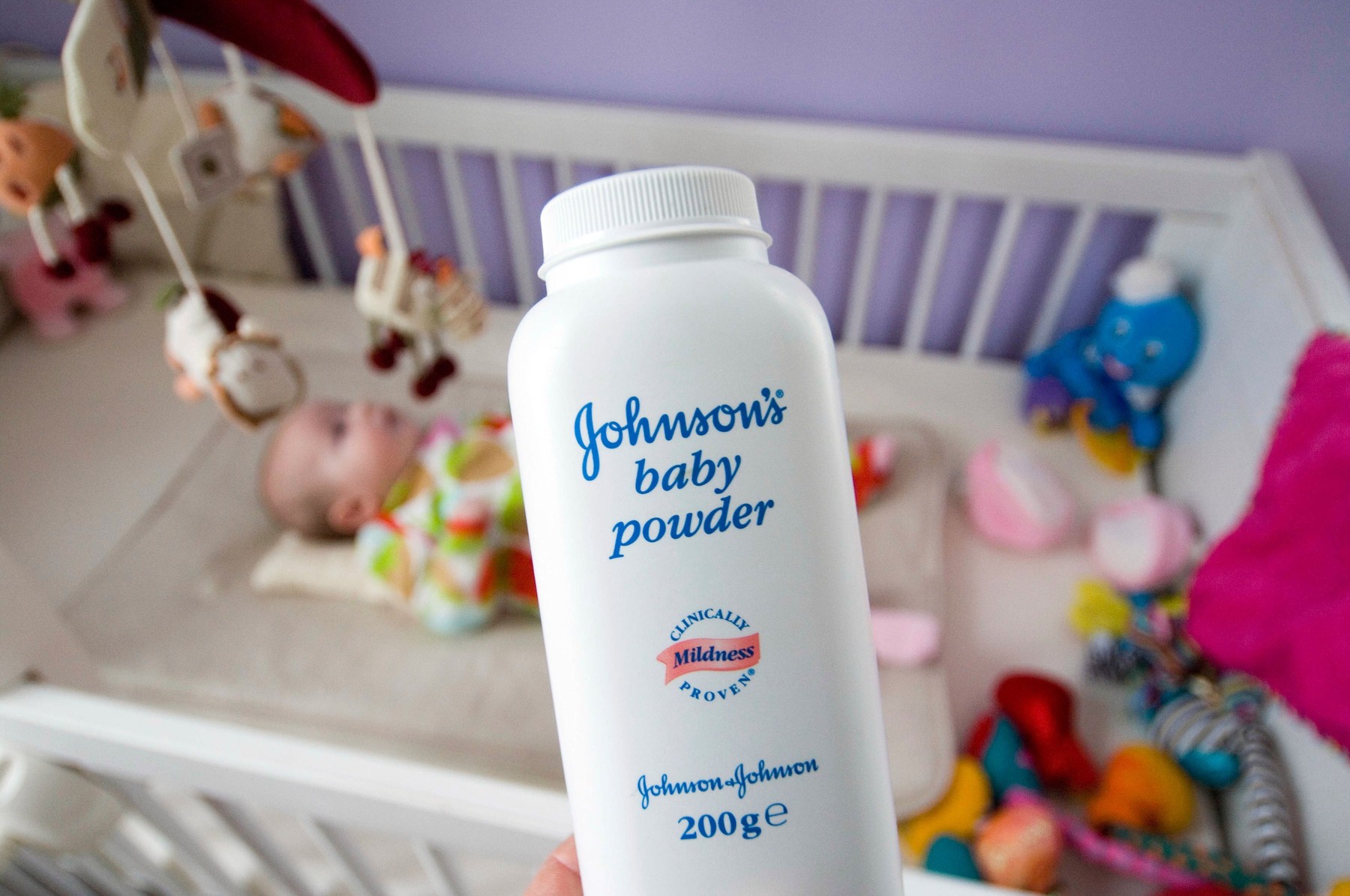Bottle of Johnsons Baby Power talc  in front of a baby in a cot.
