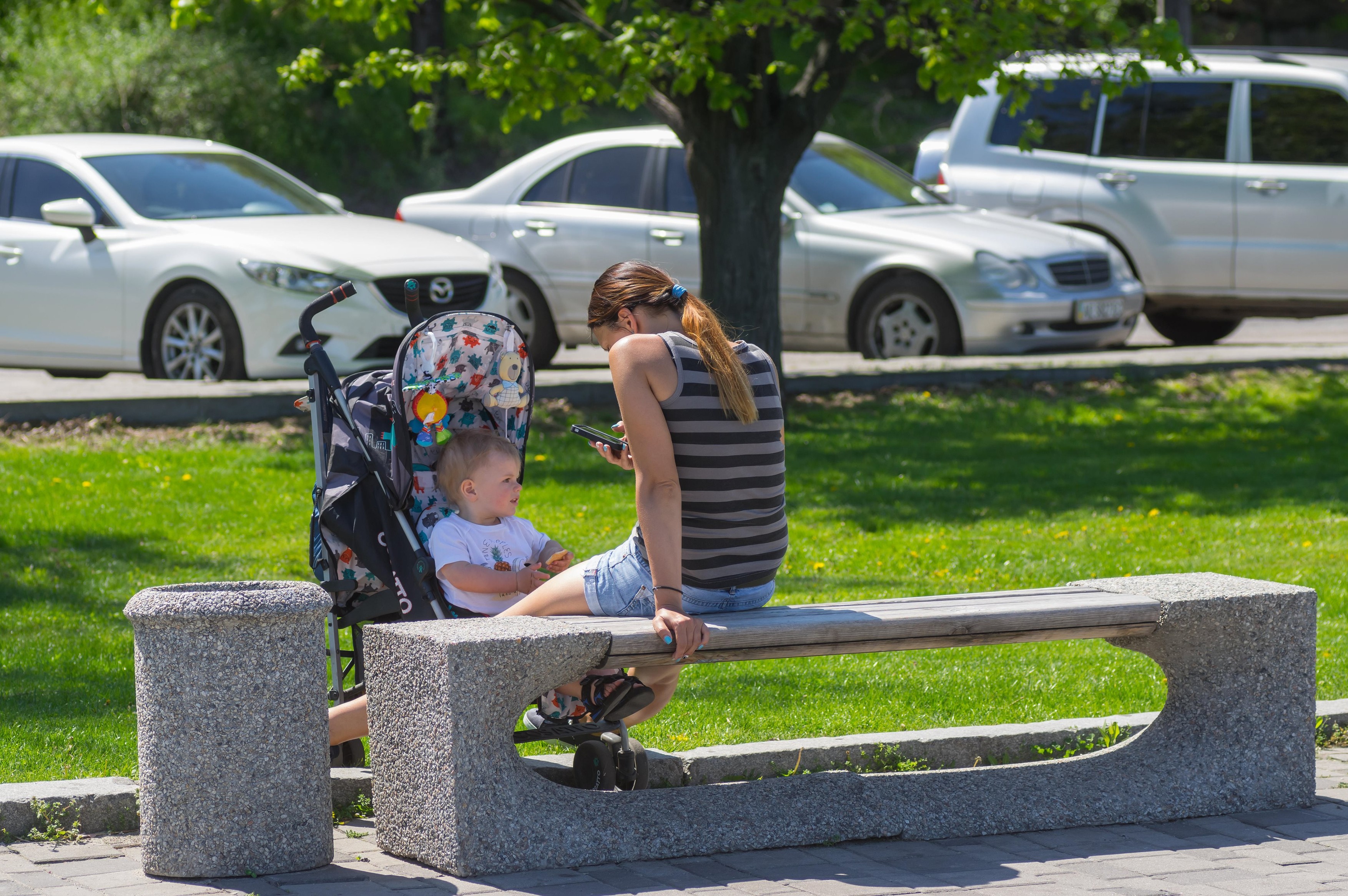 Dnipro, Ukraine - May 06, 2017: Mother sitting on a bench and looking into cellular while kid in baby carriage watching with interest as life goes on in the park Credit: Yuri Kravchenko/Alamy Live News