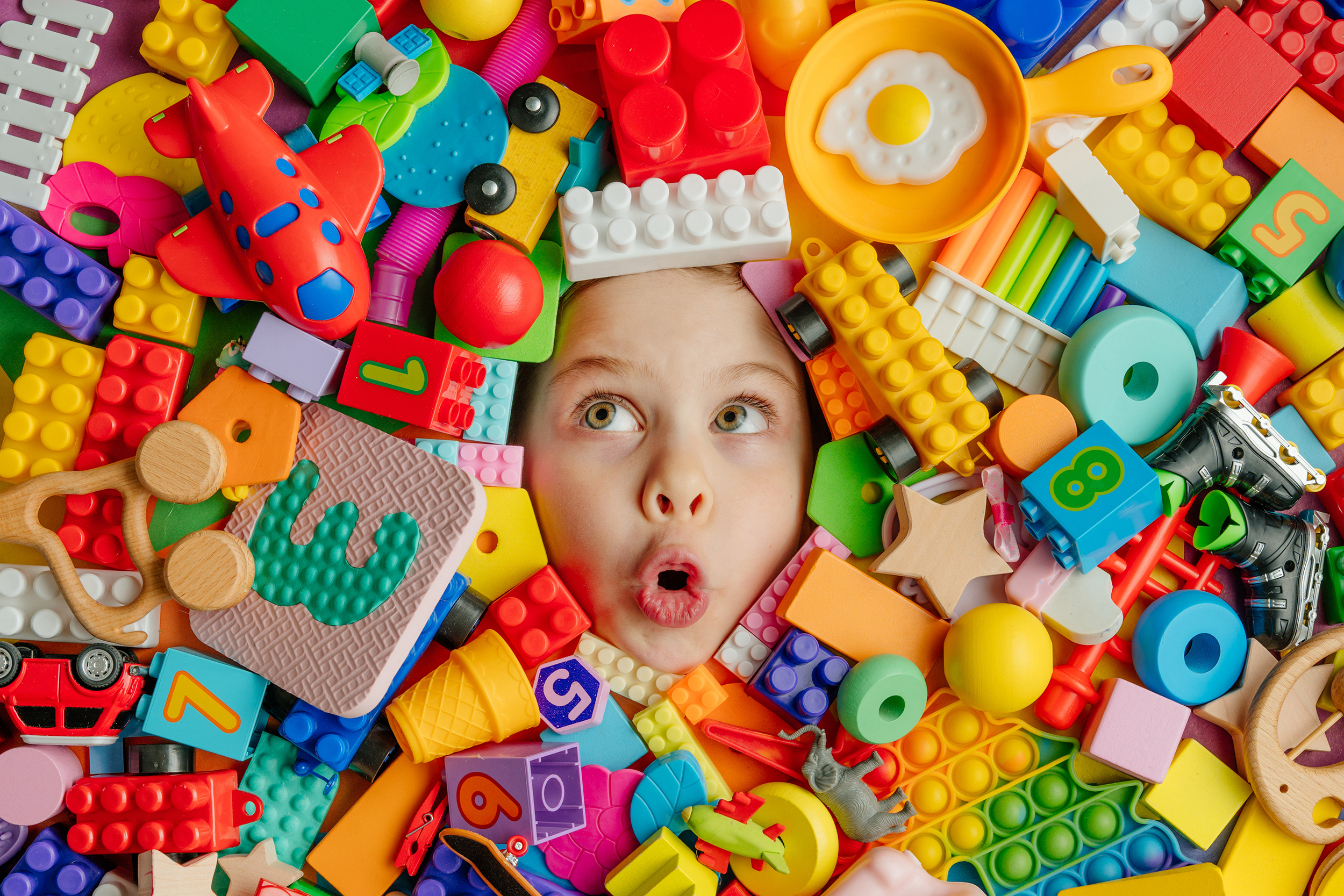 Funny,Surprised,Little,Girl,Lying,In,The,Chaos,Of,Toys.
