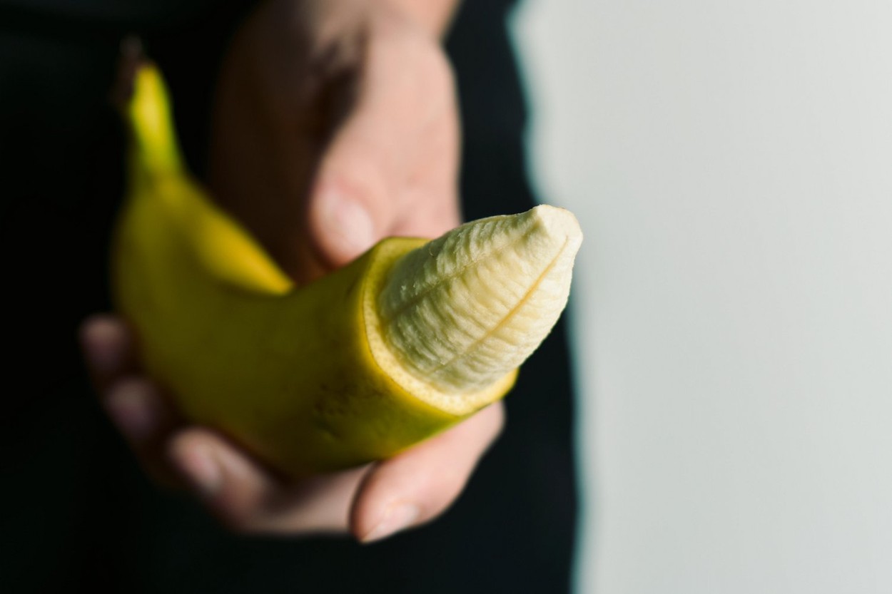 closeup of the hand of a young man with a banana with the tip of its skin removed, depicting a circumcised male member