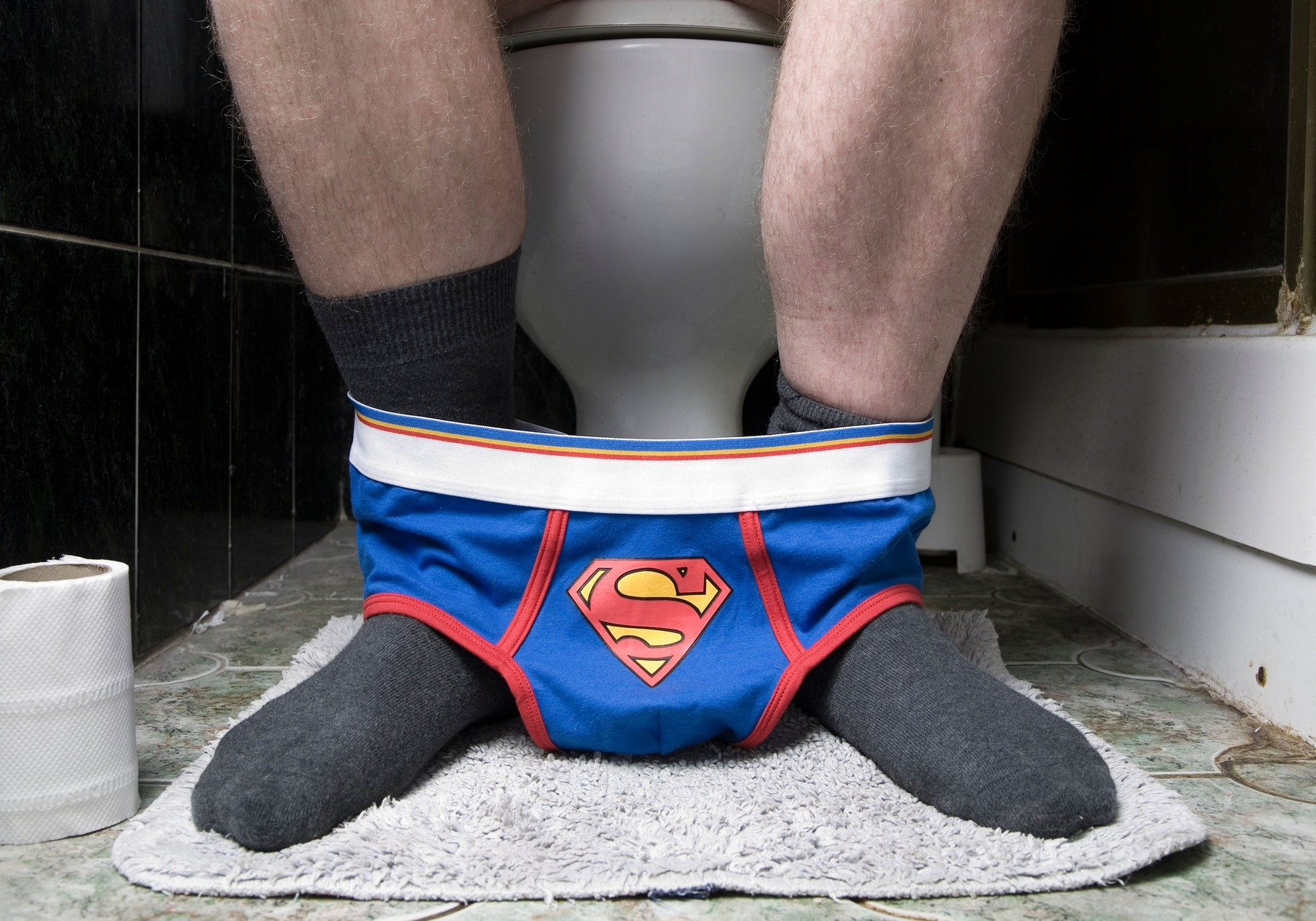 a male on the toilet with superman underpants around his ankles