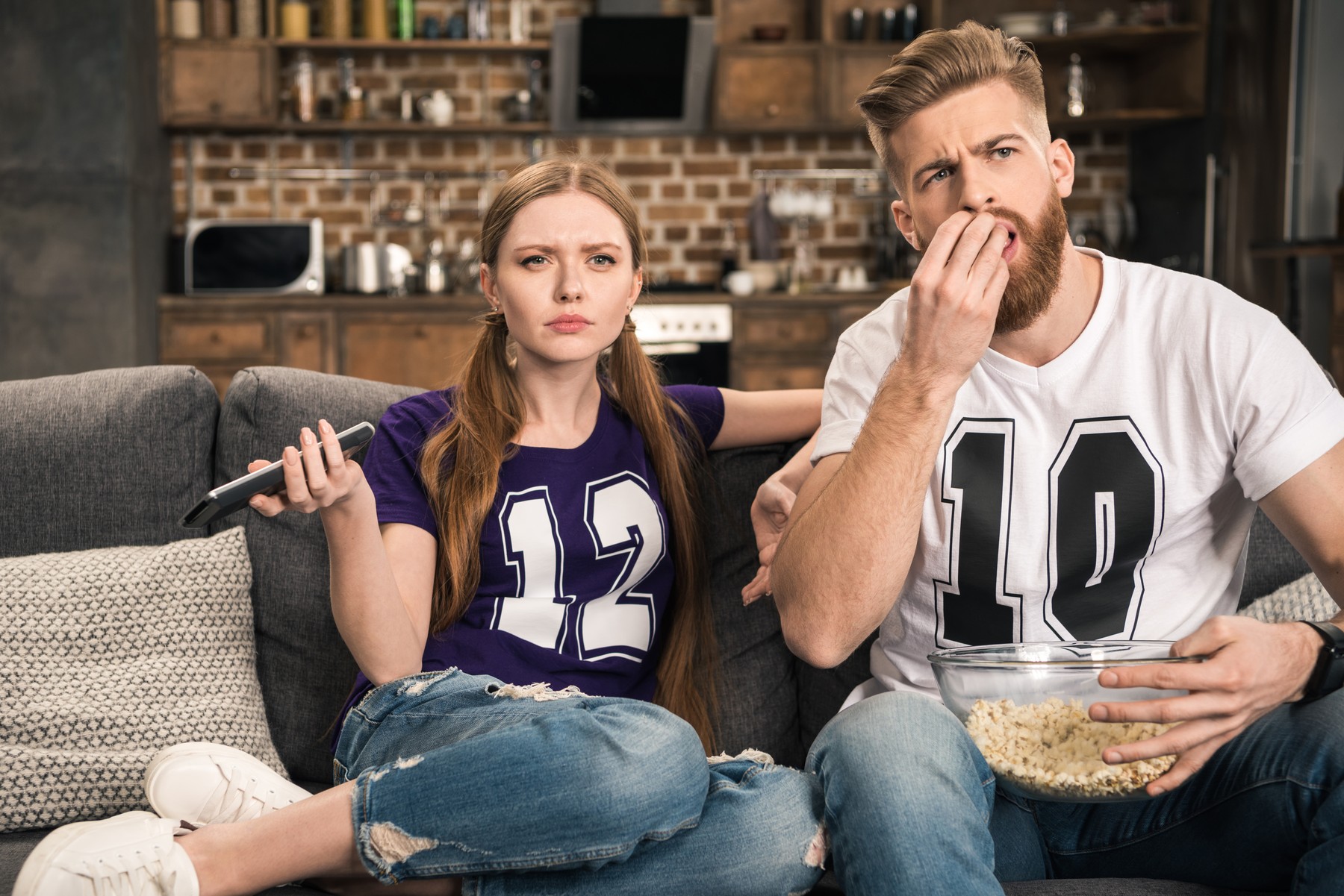 portrait of concentrated couple watching movie with popcorn at home