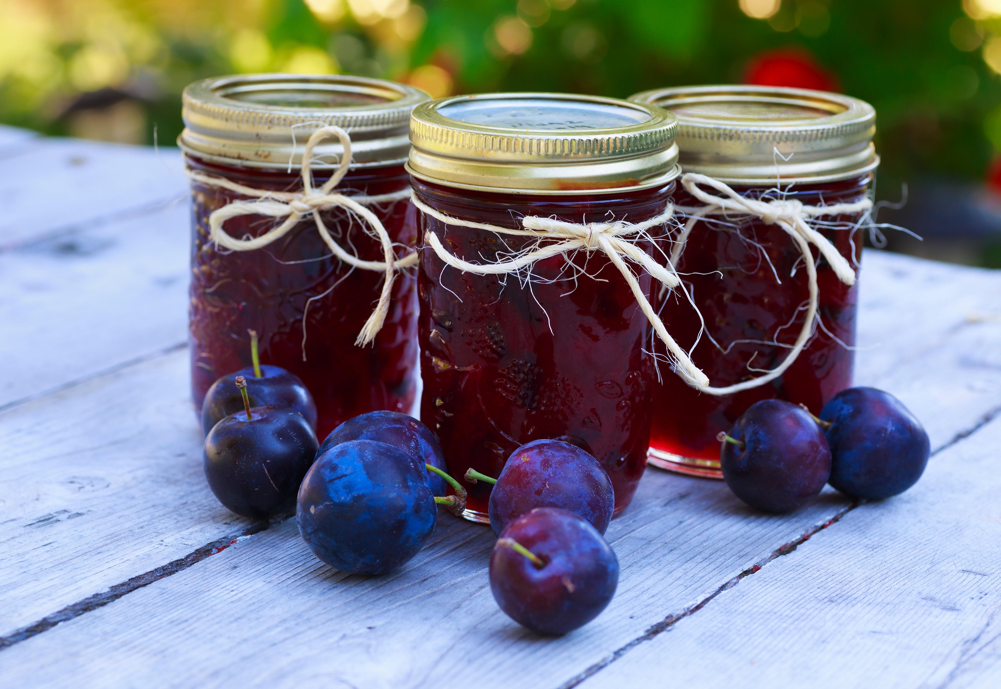 Bottles of homemade plum jam and some plums on an outside picnic table.