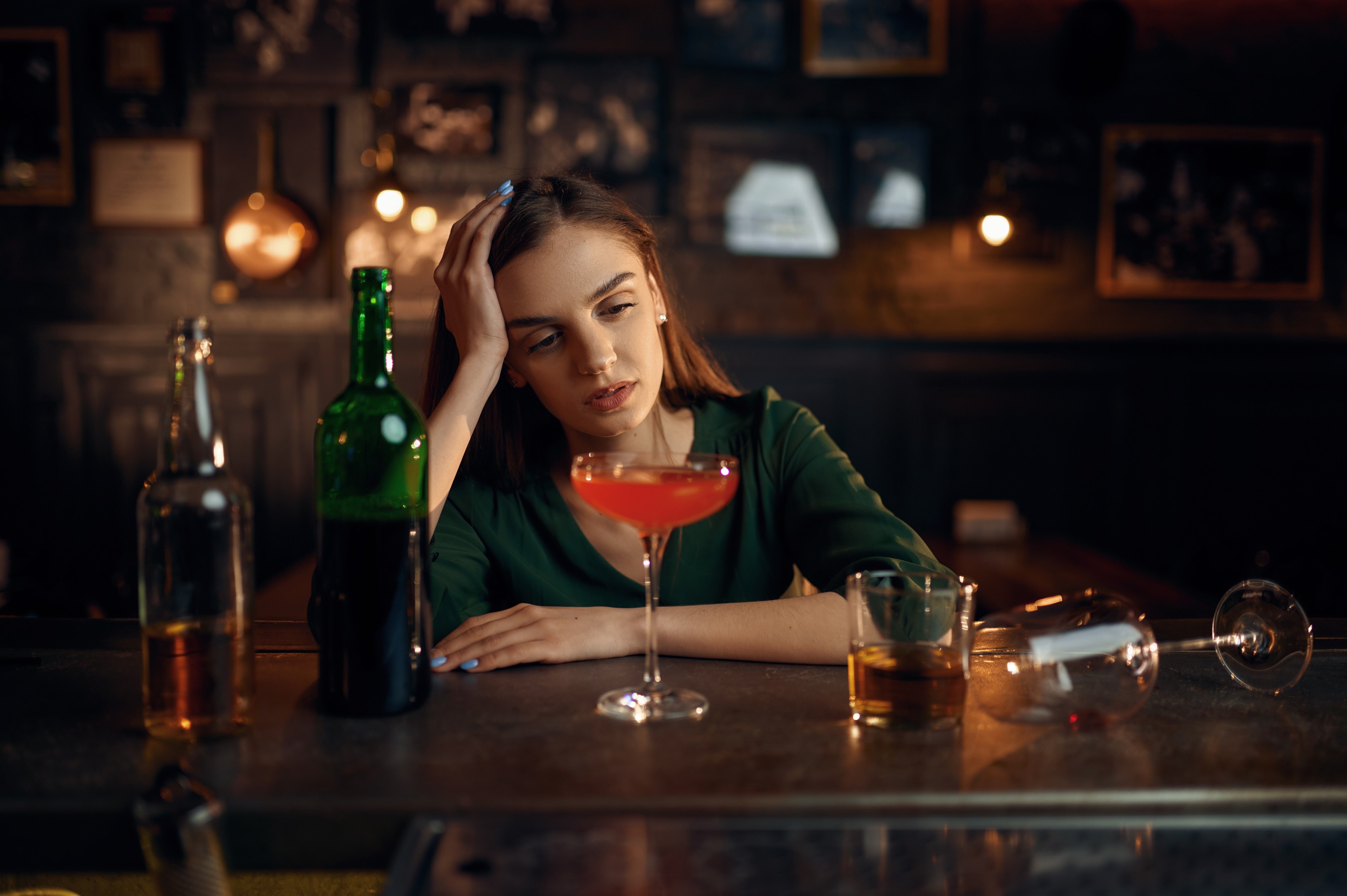 Depressed woman drinks alcohol at counter in bar