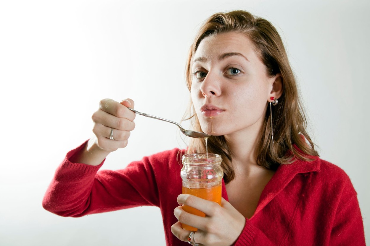 woman getting caught while eating honey from a jar with a spoon
