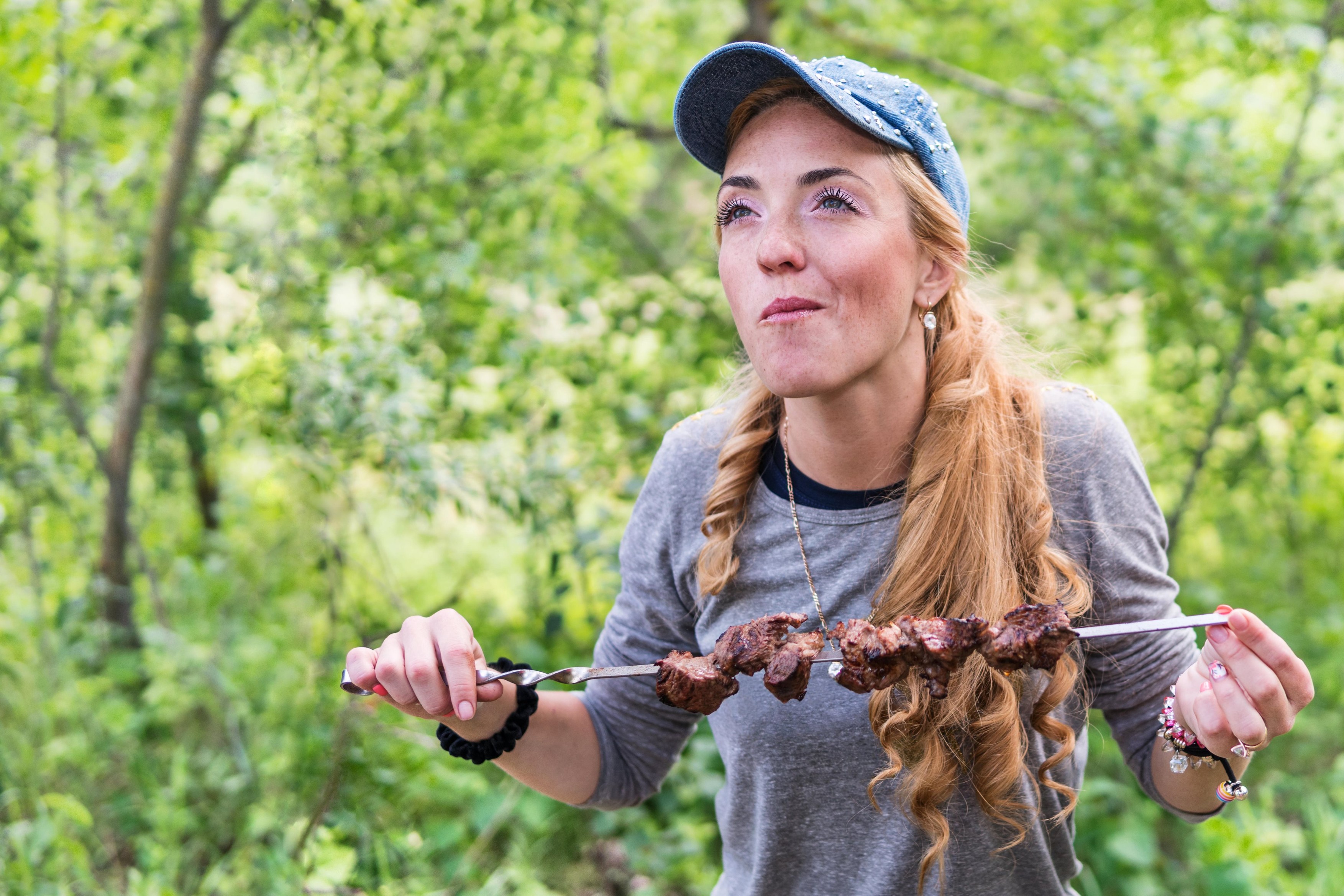 Freckled woman with pleasure eating meat on a skewer in the nature