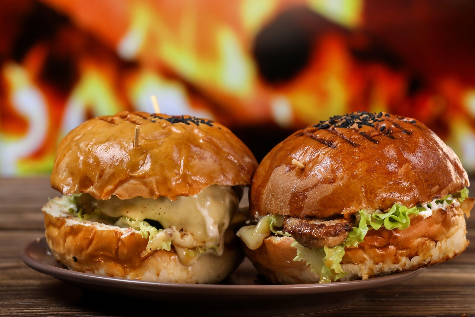 Two freshly fried burgers lie on a plate and a wooden table against the background of a fireplace.