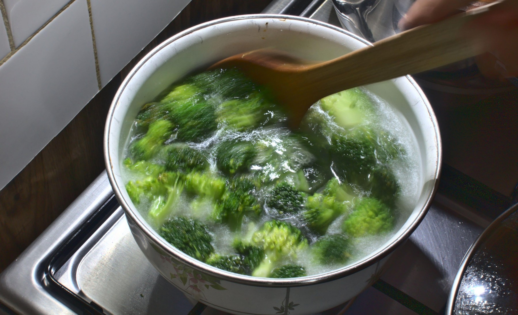 Woman is stirring broccoli soup on the kitchen stove with a wooden spoon, healthy living, fresh green vegetables