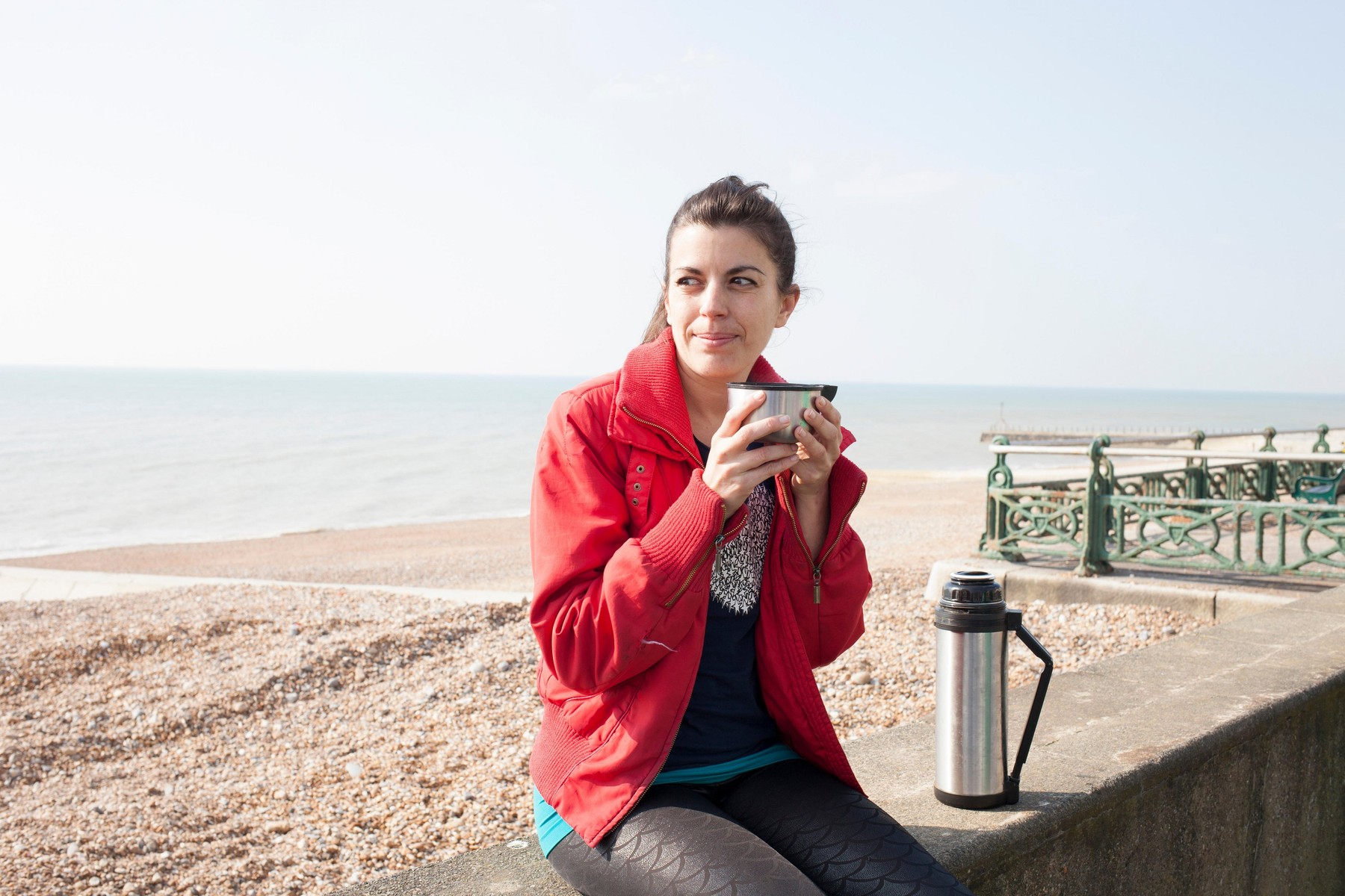 Female runner taking a coffee break on wall at Brighton beach