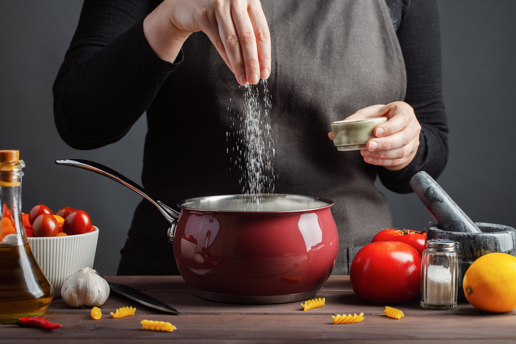 The chef preparations spaghetti and pasta, salt water, against a dark background, the concept of cooking. Woman salting water before cooking pasta fus