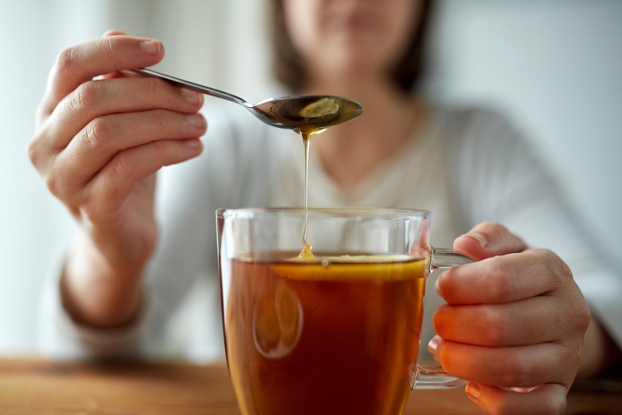 close up of woman adding honey to tea with lemon