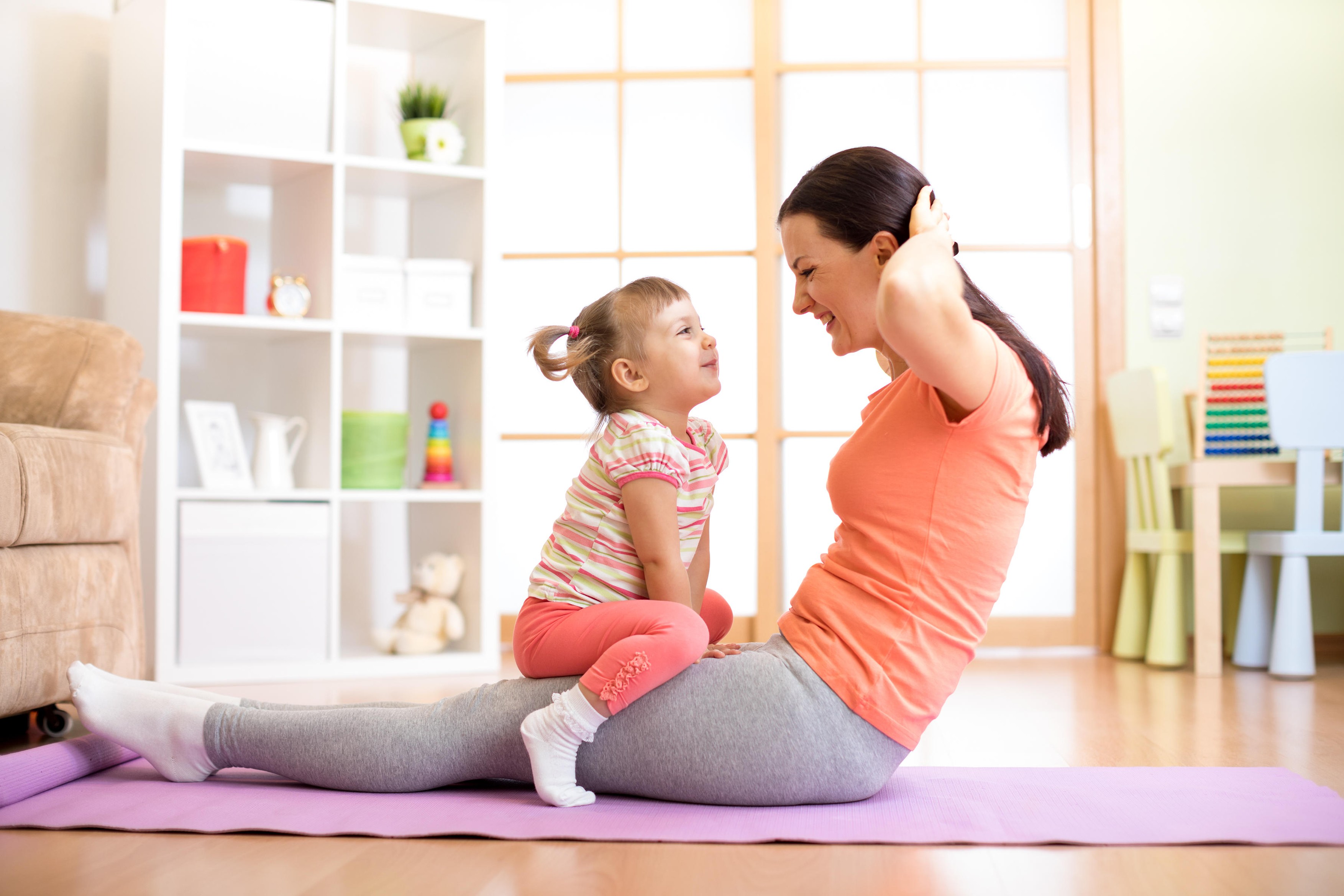 Mother and child daughter are engaged in fitness, yoga, exercise at home. Kid and woman swing press on stomach.
