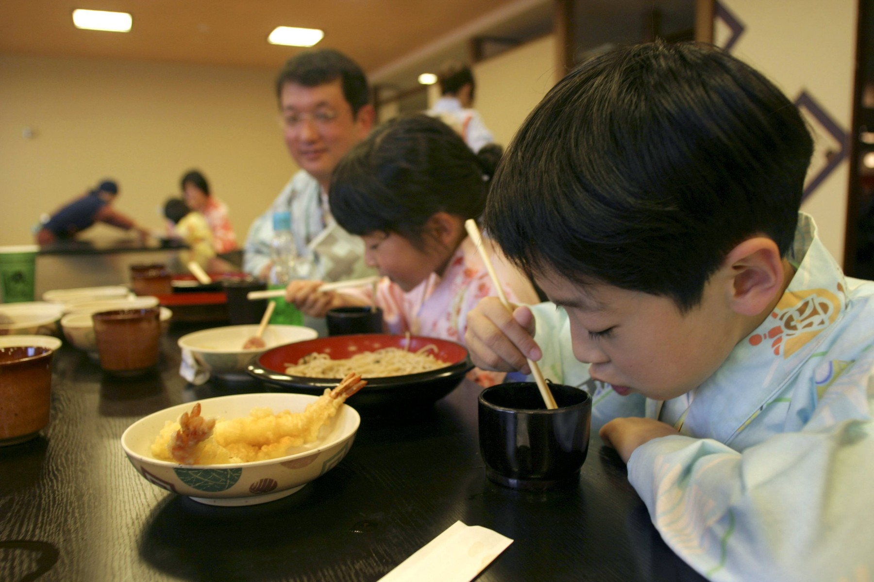 Japanese family eating noodles with chopsticks, at a spa resort, Tokyo, Japan.