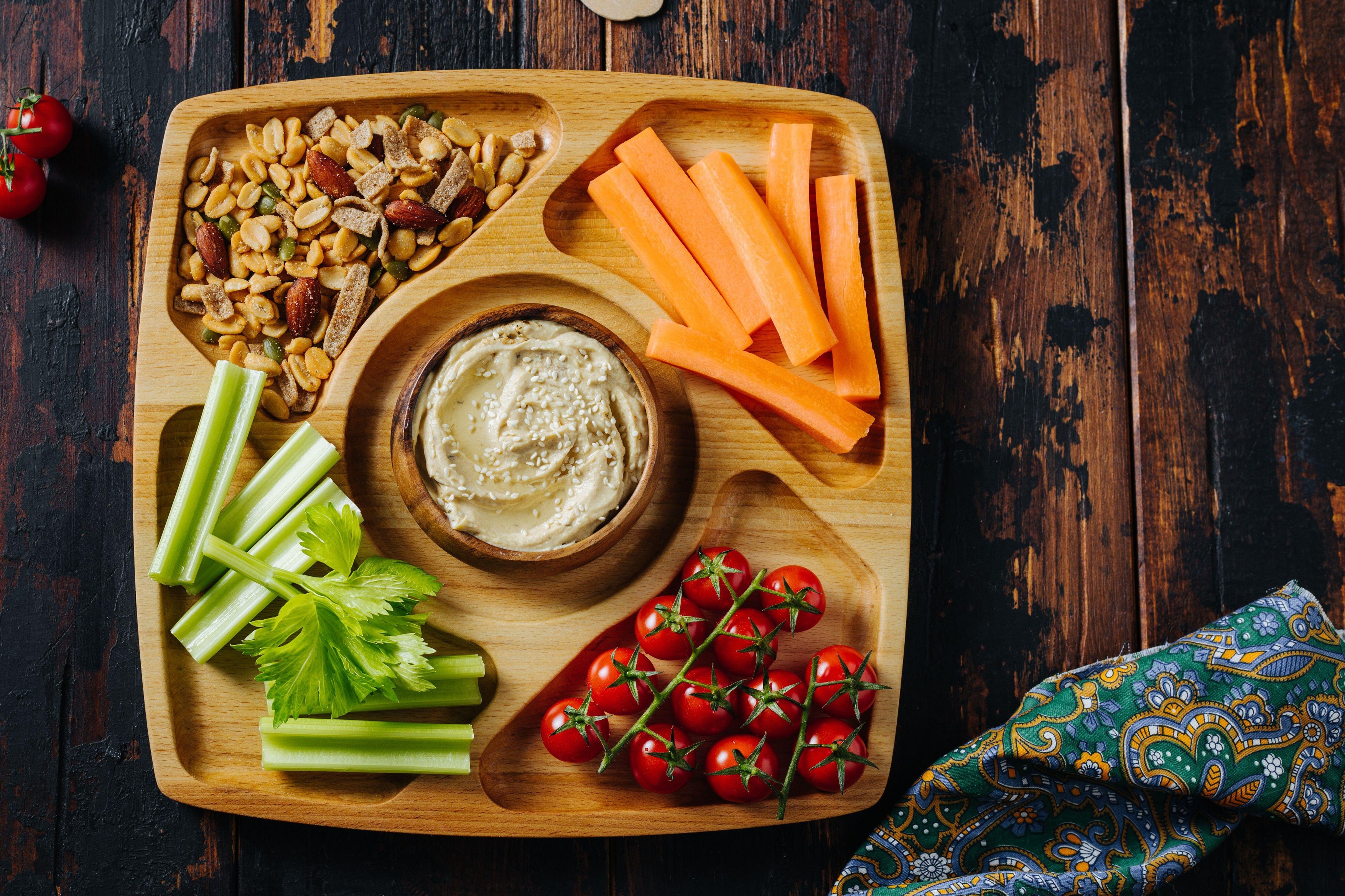 Hummus and vegetable sticks of carrot and celery on a wooden plate