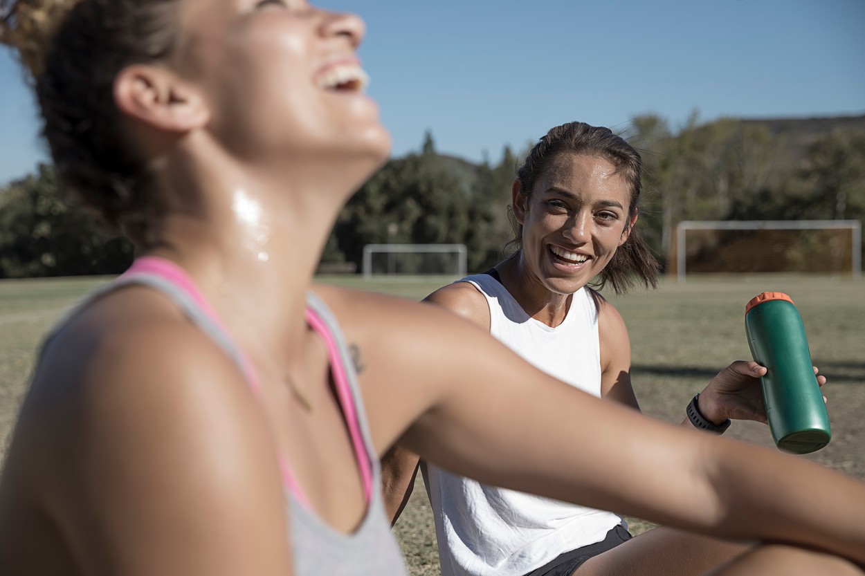 Women sitting on football pitch drinking from water bottle