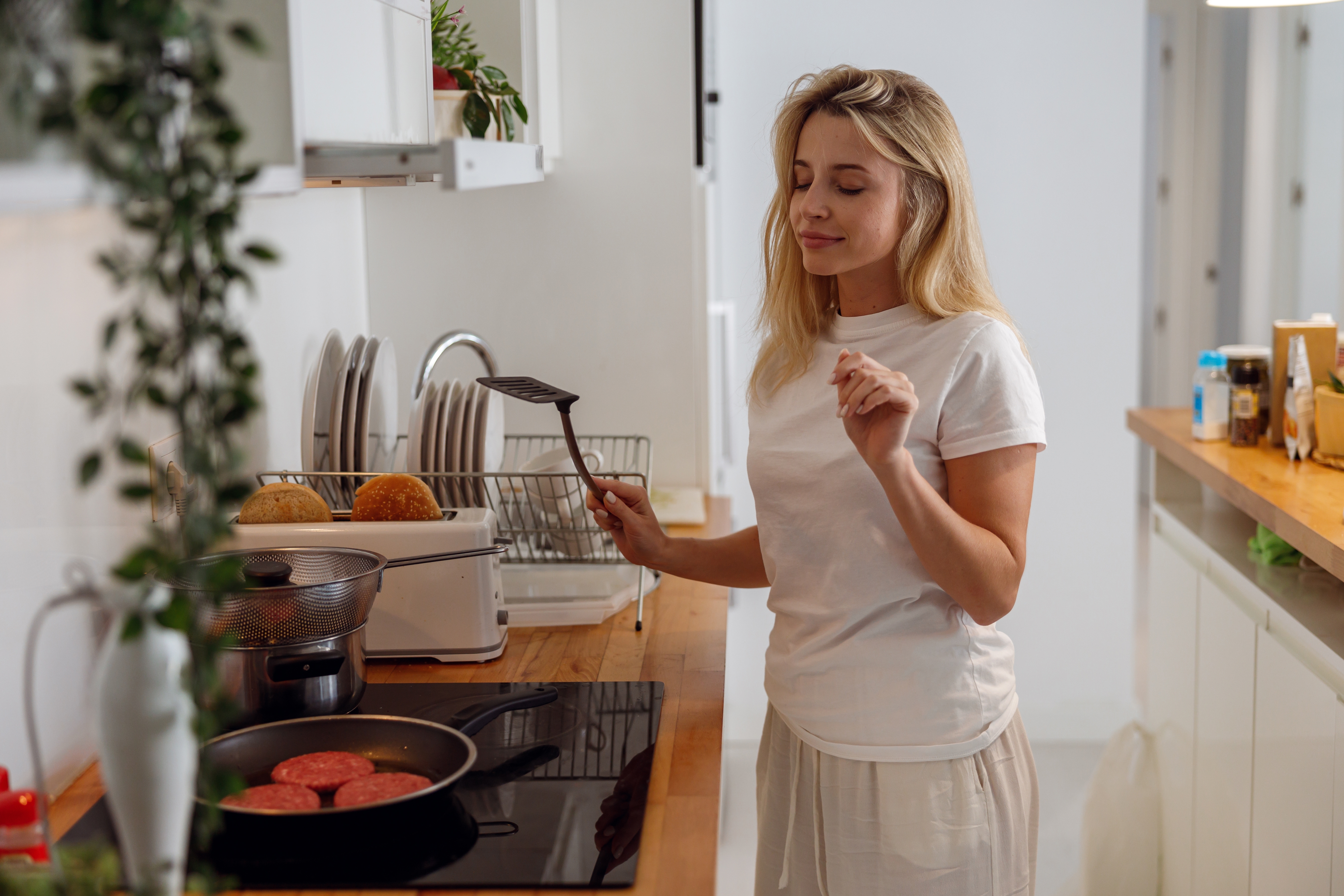 Pretty,Young,Female,Standing,With,Spatula,At,Kitchen,And,Frying