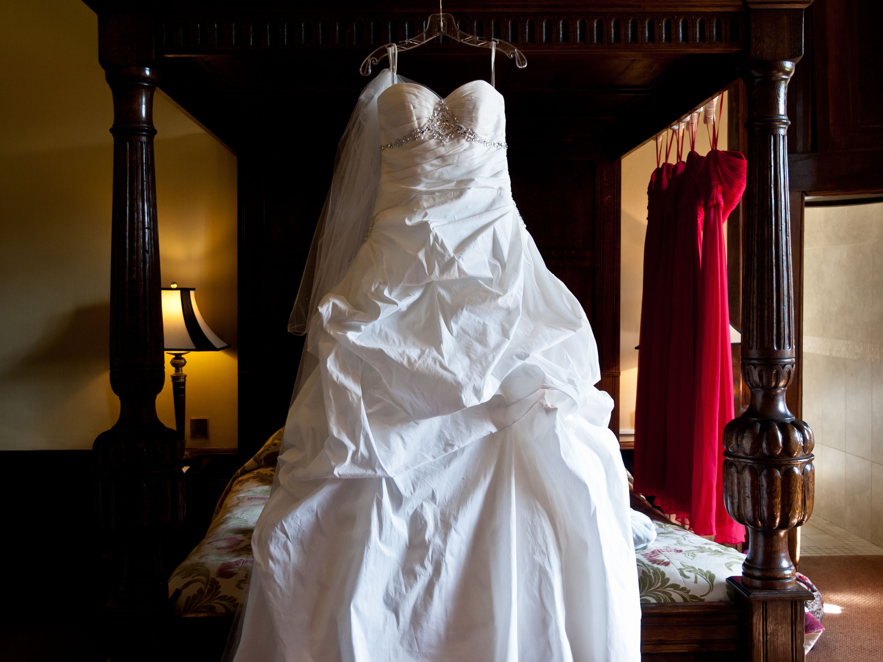 A traditional white wedding dress hangs from a four-poster bed