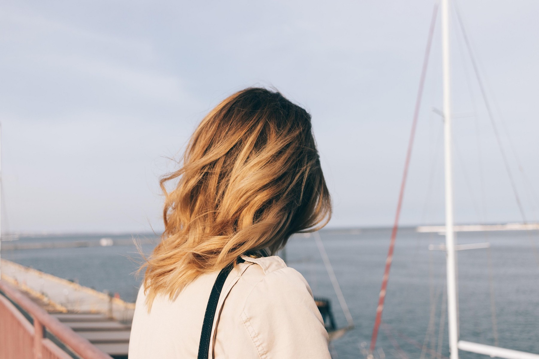 Rear view close-up young woman looking at the sea. Female head with golden honey color wavy hairstyle watch at the seaport and the waterfront.