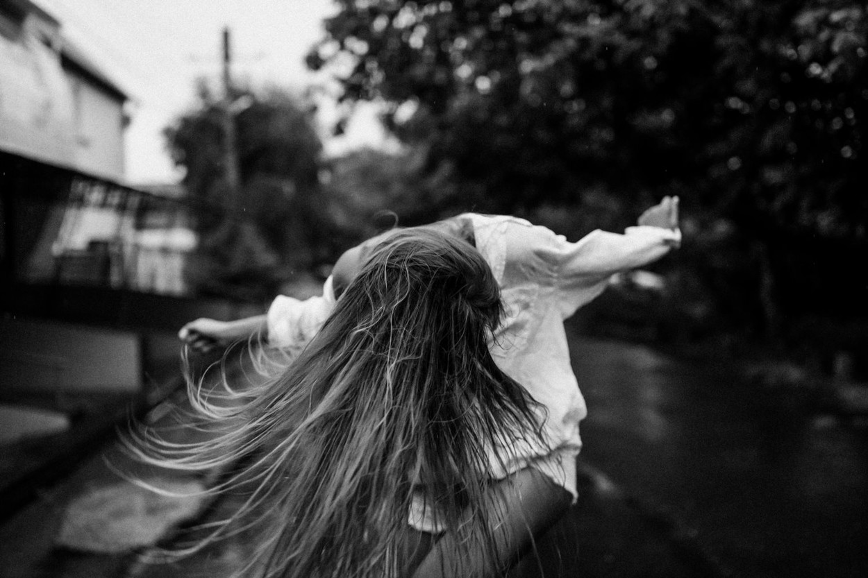Wild girl having fun outdoor under the warm summer rain in a oversize white shirt and short jeans. Her hands behind, she jumping and dancing. Enjoys