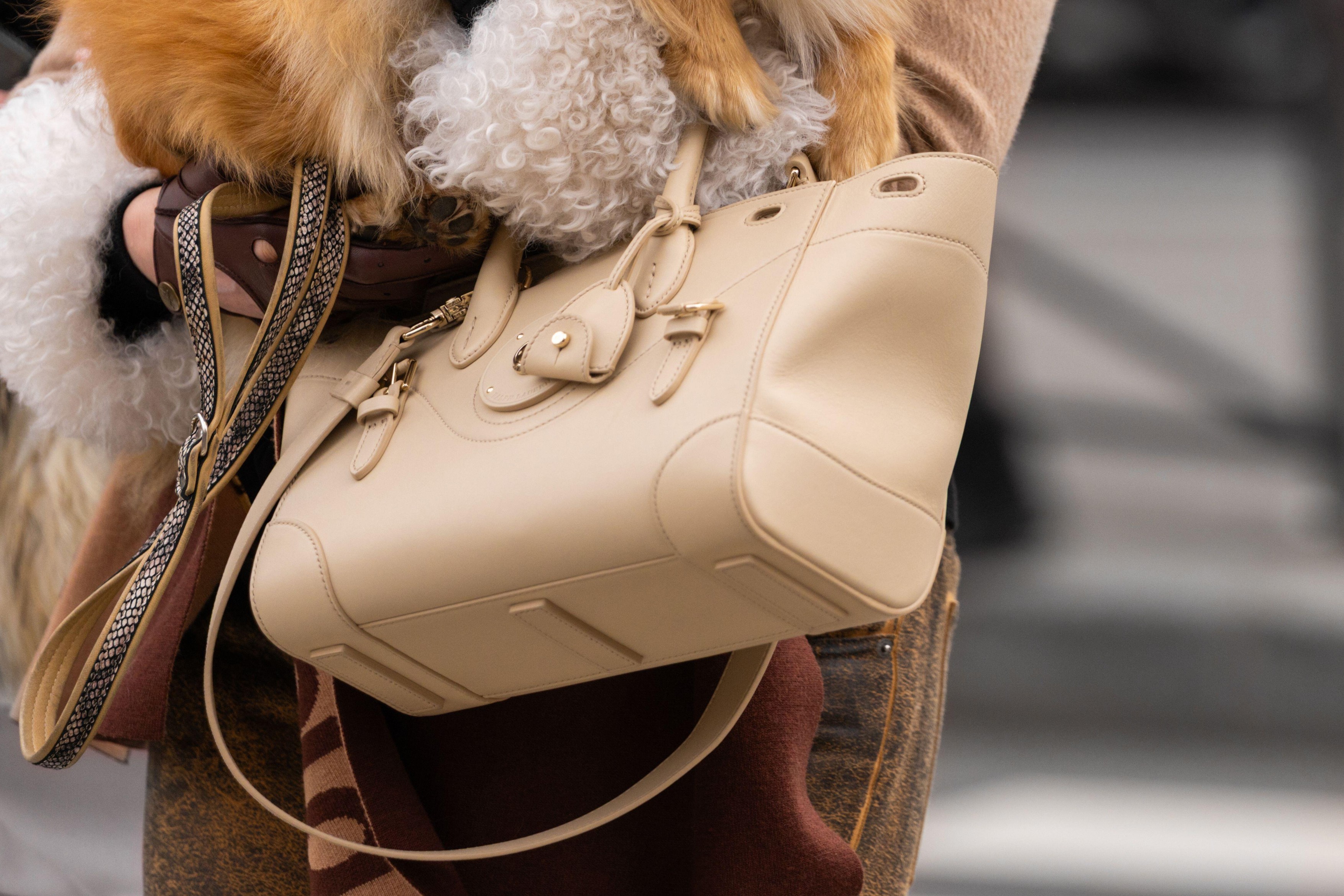 Paris, France - March 11, 2025: Cream leather Ralph Lauren ricky 27 satchel bag with gold accents. Neutral shearling and fox fur coat outfit. Street