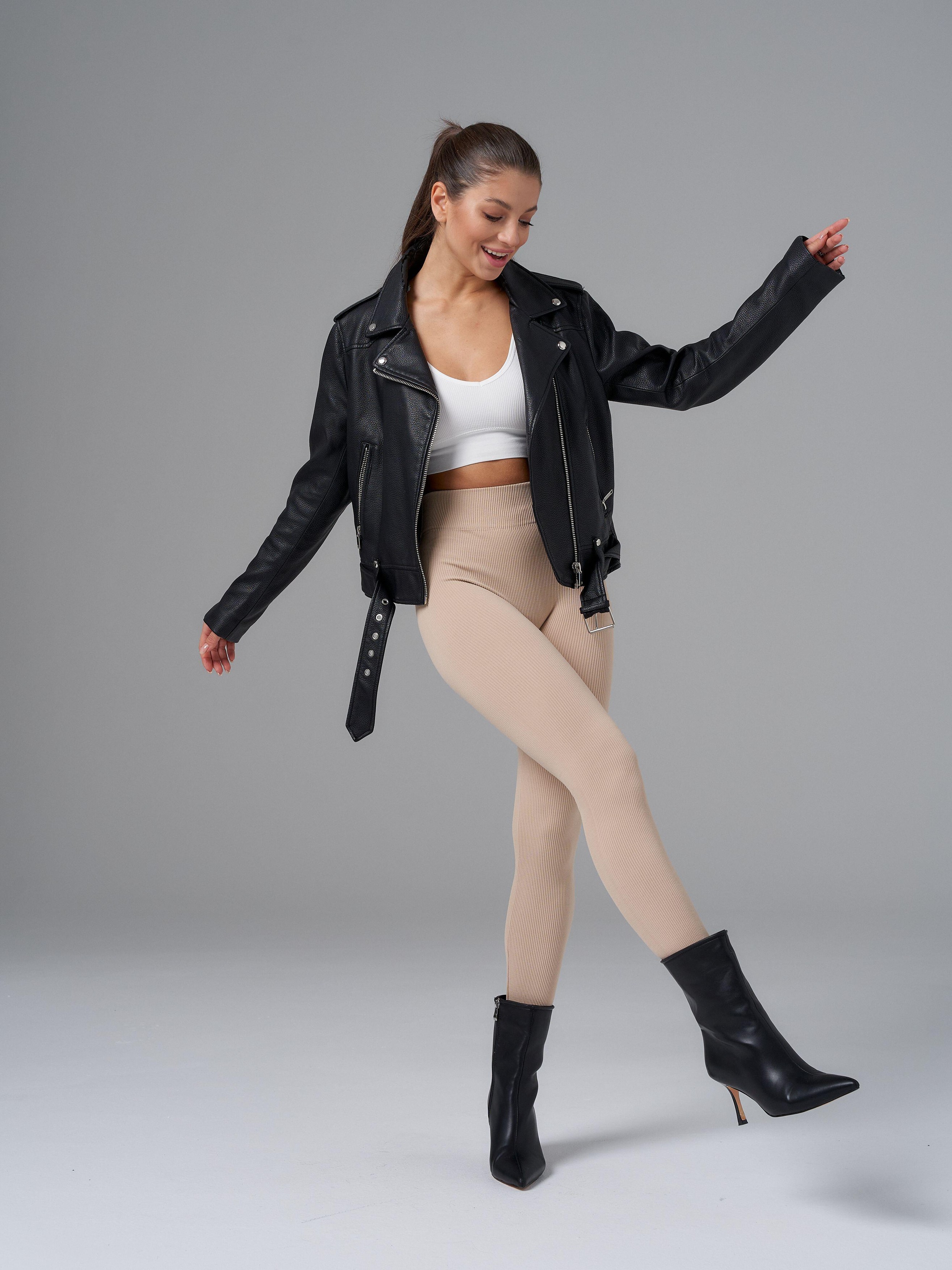 A woman smiling and posing confidently, wearing a black leather jacket,