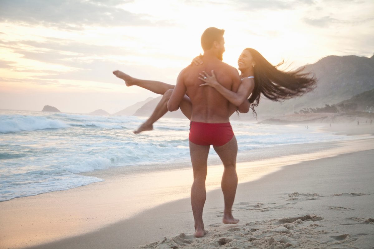 Парень несёт девушку на руках на пляже